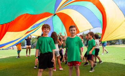 Kids playing in a field under a colorful parachute